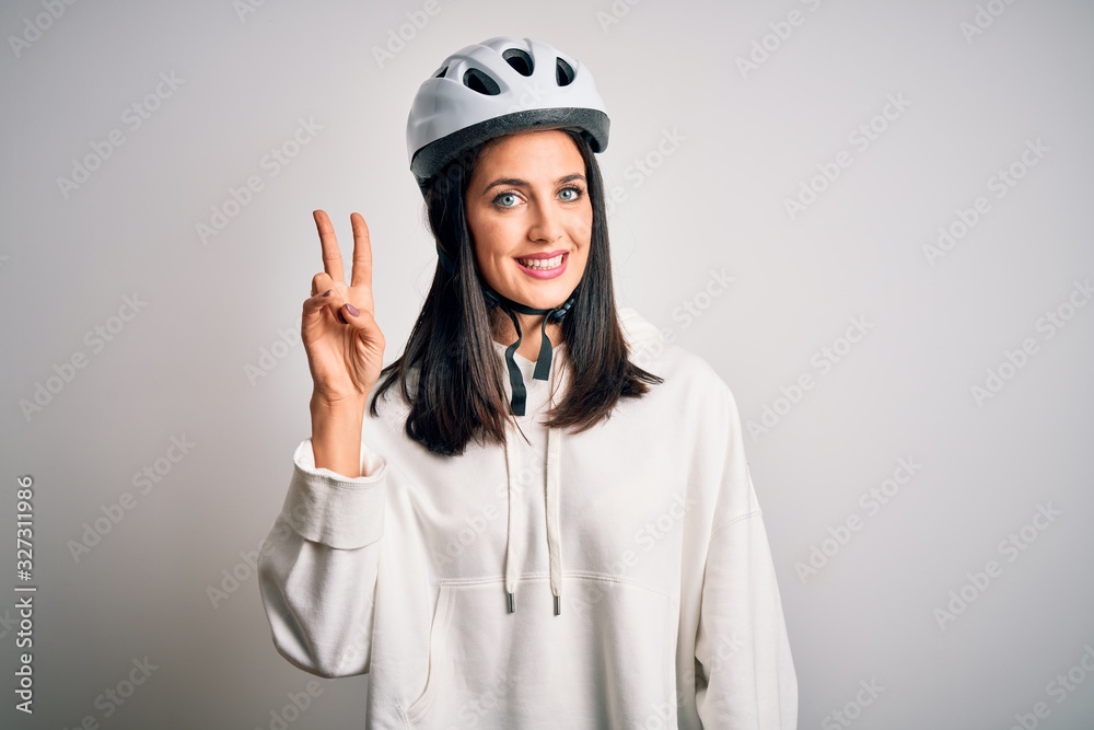 Young cyclist woman with blue eyes wearing bike helmet over isolated white background smiling with happy face winking at the camera doing victory sign. Number two. Young cyclist woman with blue eyes wearing bike helmet over isolated white background smiling with happy face winking at the camera doing victory sign. Number two.