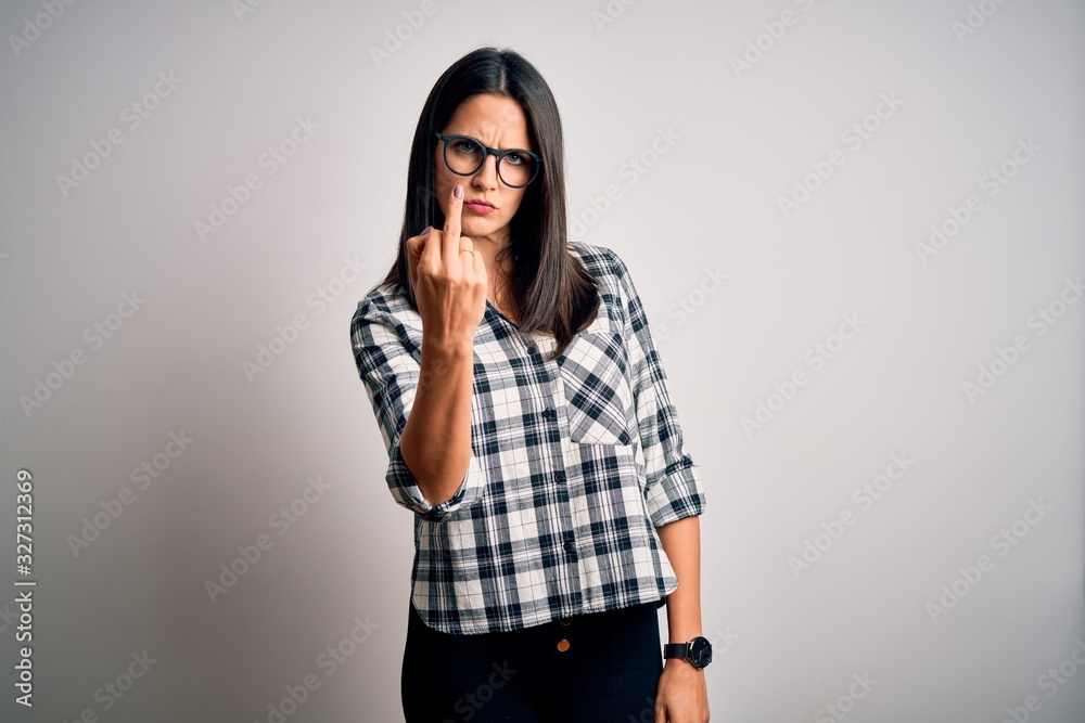 Young brunette woman with blue eyes wearing casual shirt and glasses over white background Showing middle finger, impolite and rude fuck off expression Young brunette woman with blue eyes wearing casual shirt and glasses over white background Showing middle finger, impolite and rude fuck off expression