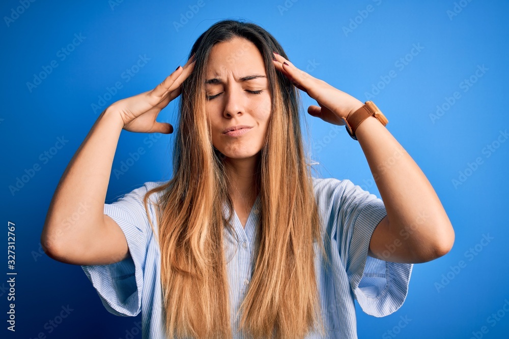 Fototapeta premium Young beautiful blonde woman with blue eyes wearing striped shirt over blue background suffering from headache desperate and stressed because pain and migraine. Hands on head.