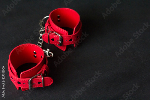 Red leather handcuffs on black background. Adult games and toys. BDSM, bondage play, fetish wear and kinky sex toy concept with close up