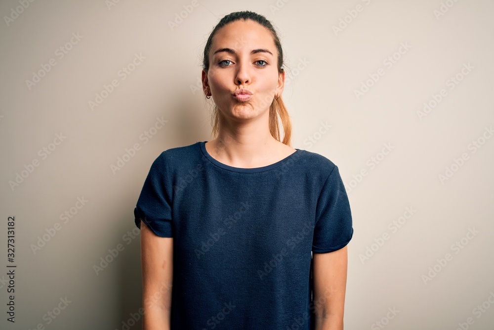 Young beautiful blonde woman with blue eyes wearing casual t-shirt over white background making fish face with lips, crazy and comical gesture. Funny expression. Young beautiful blonde woman with blue eyes wearing casual t-shirt over white background making fish face with lips, crazy and comical gesture. Funny expression.