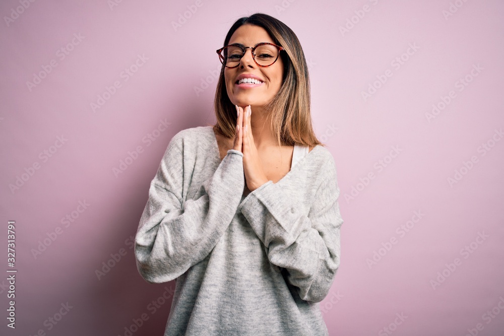 Young beautiful brunette woman wearing casual sweater and glasses over pink background praying with hands together asking for forgiveness smiling confident.