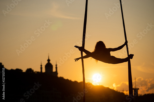 Silhouette of a flexible woman acrobat on aerial silk during a sunset on Kiev city background. concept of freedom and peace