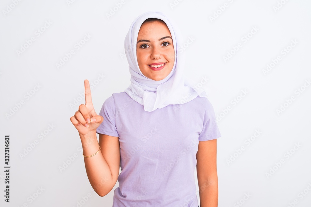 Young beautiful arabian girl wearing hijab standing over isolated white background showing and pointing up with finger number one while smiling confident and happy.