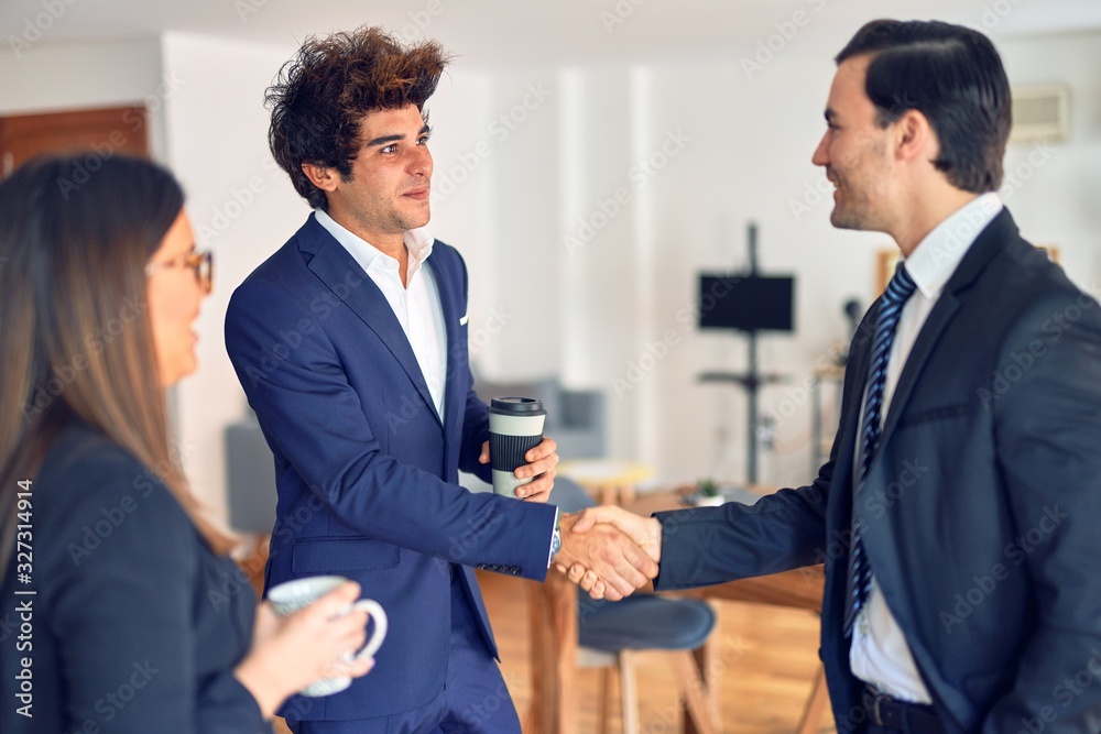 Young beautiful group of business workers smiling happy and confident. Standing with smile on face drinking coffee and shaking hands for agreement at the office Young beautiful group of business workers smiling happy and confident. Standing with smile on face drinking coffee and shaking hands for agreement at the office