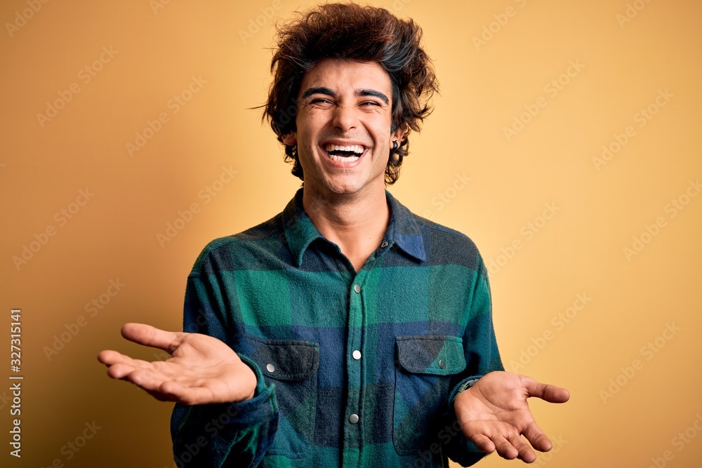 Young handsome man wearing casual shirt standing over isolated yellow background smiling cheerful with open arms as friendly welcome, positive and confident greetings Young handsome man wearing casual shirt standing over isolated yellow background smiling cheerful with open arms as friendly welcome, positive and confident greetings