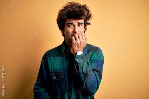 Young handsome man wearing casual shirt standing over isolated yellow background looking stressed and nervous with hands on mouth biting nails. Anxiety problem. © Krakenimages.com
