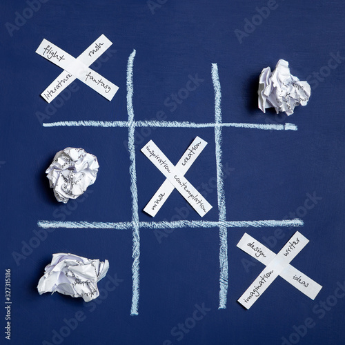Conceptual photo. The torment of creativity. Tic-tac-toe game. Crumpled sheets of paper on a blue background and paper crosses. Flat lay, top view.