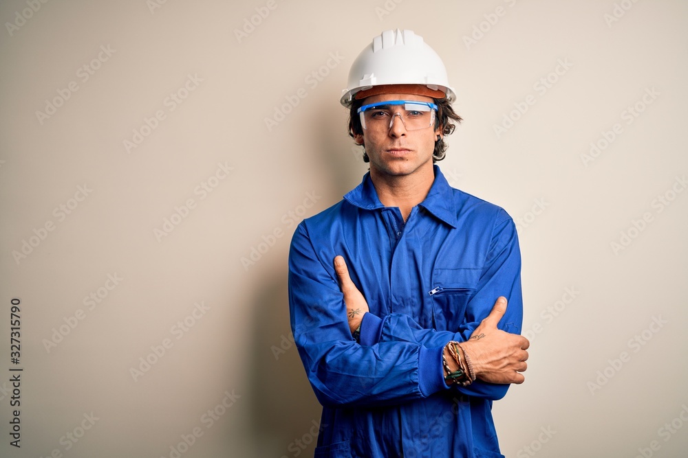 Young constructor man wearing uniform and security helmet over isolated white background skeptic and nervous, disapproving expression on face with crossed arms. Negative person.
