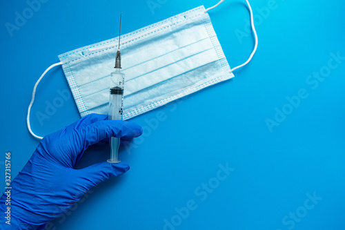 Hand in a medical glove holding a syringe with a vaccine medical mask on a blue background. The vaccine for coronavirus concept