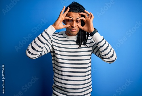 Young handsome african american afro man with dreadlocks wearing casual striped sweater Trying to open eyes with fingers, sleepy and tired for morning fatigue