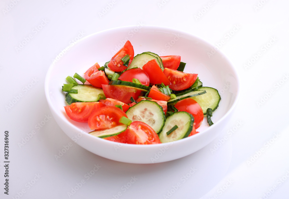 Tomato and cucumber salad with green onions in a white plate on a white background