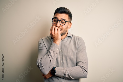 Young handsome man wearing elegant shirt and glasses over isolated white background looking stressed and nervous with hands on mouth biting nails. Anxiety problem.