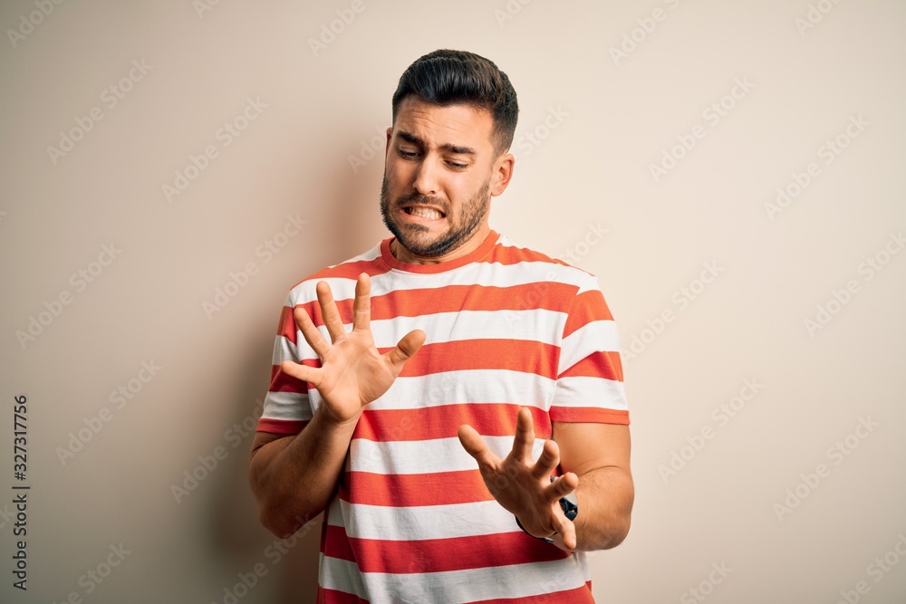 Young handsome man wearing casual striped t-shirt standing over isolated white background disgusted expression, displeased and fearful doing disgust face because aversion reaction.
