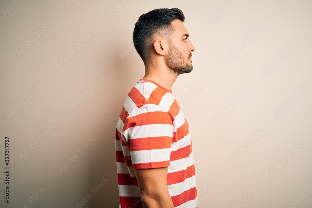 Young handsome man wearing casual striped t-shirt standing over isolated white background looking to side, relax profile pose with natural face and confident smile. Young handsome man wearing casual striped t-shirt standing over isolated white background looking to side, relax profile pose with natural face and confident smile.