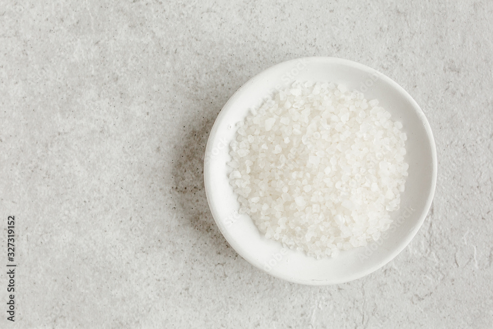 Salt in a bowl on gray stone table. Sea salt flat lay, top view. Spa skincare concept. Natural/Organic spa cosmetics products