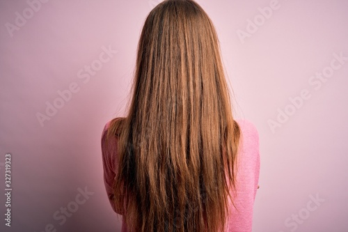 Young beautiful redhead woman wearing casual sweater over isolated pink background standing backwards looking away with crossed arms