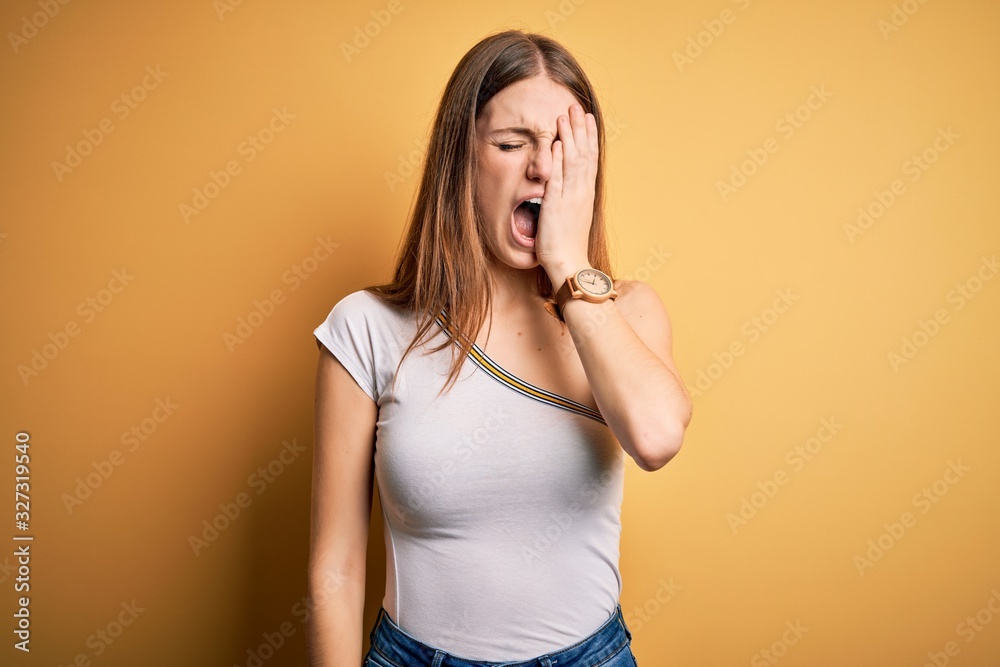 Young beautiful redhead woman wearing casual t-shirt over isolated yellow background Yawning tired covering half face, eye and mouth with hand. Face hurts in pain. Young beautiful redhead woman wearing casual t-shirt over isolated yellow background Yawning tired covering half face, eye and mouth with hand. Face hurts in pain.