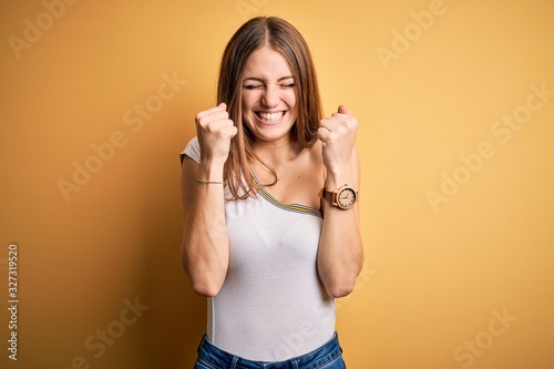 Young beautiful redhead woman wearing casual t-shirt over isolated yellow background excited for success with arms raised and eyes closed celebrating victory smiling. Winner concept.