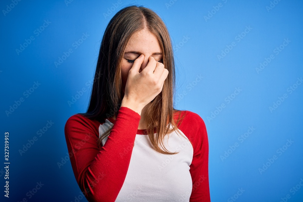 Young beautiful redhead woman wearing casual t-shirt over isolated blue background tired rubbing nose and eyes feeling fatigue and headache. Stress and frustration concept.