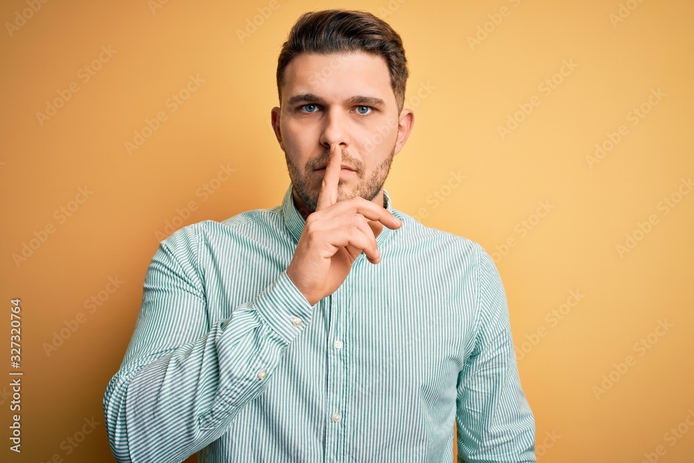 Young business man with blue eyes wearing elegant green shirt over yellow background asking to be quiet with finger on lips. Silence and secret concept. Young business man with blue eyes wearing elegant green shirt over yellow background asking to be quiet with finger on lips. Silence and secret concept.