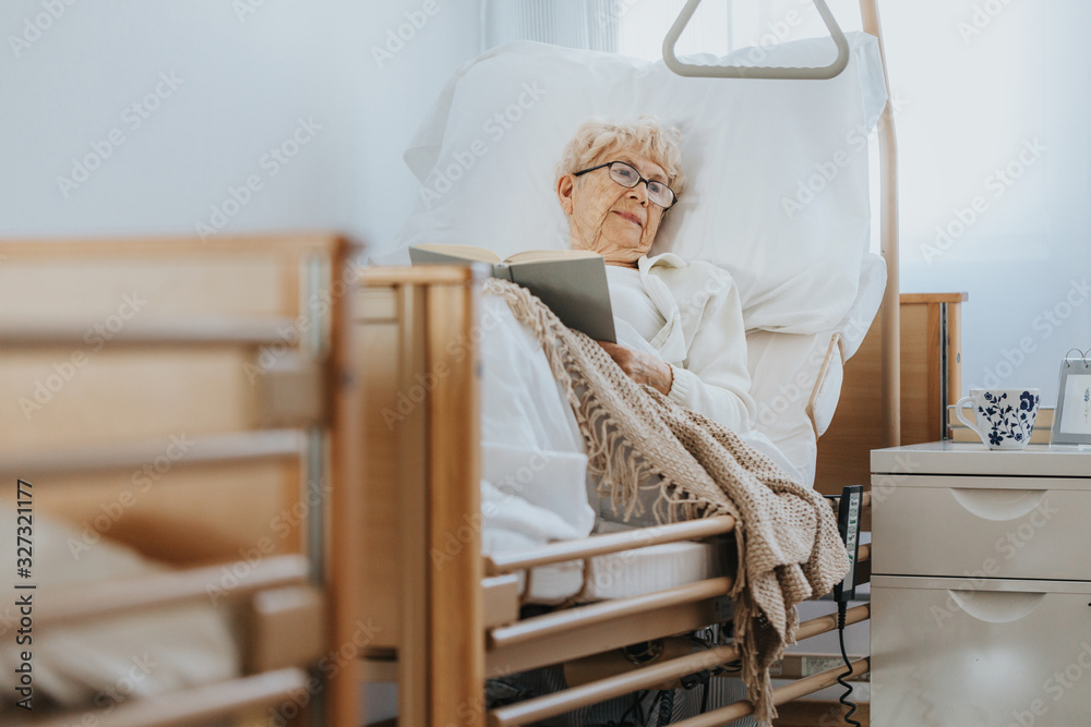 © Photographee.eu - Sick senior woman lies in a hospital bed and reads a book