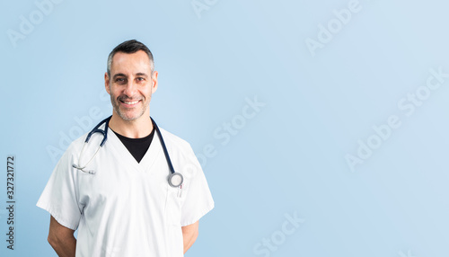 Handsome middle aged male doctor wearing white coat in front of blue wall, closeup