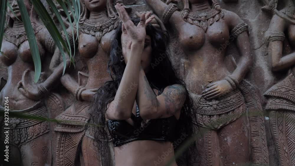 Dancing seductive woman sensually posing in slow motion on the wall with apsara statue at asian ancient temple
