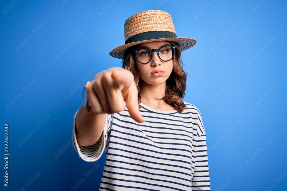 Young beautiful blonde girl wearing glasses and hat over blue isolated background pointing with finger to the camera and to you, hand sign, positive and confident gesture from the front Young beautiful blonde girl wearing glasses and hat over blue isolated background pointing with finger to the camera and to you, hand sign, positive and confident gesture from the front