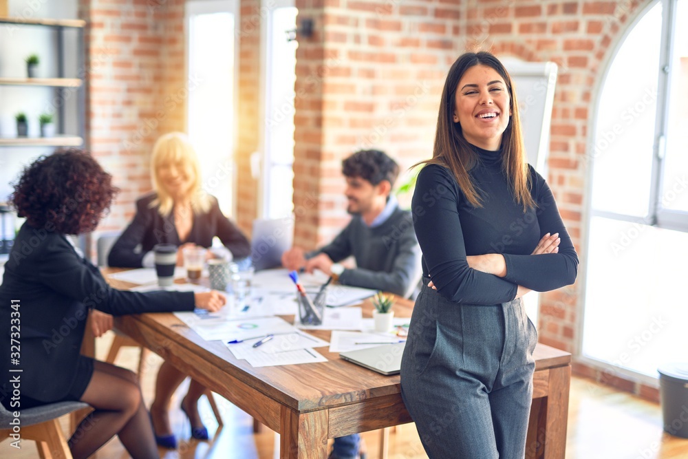 Group of business workers working together. Young beautiful woman standing smiling happy looking at the camera at the office Group of business workers working together. Young beautiful woman standing smiling happy looking at the camera at the office