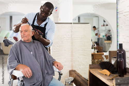 Aged male client getting haircut from African hairstylist
