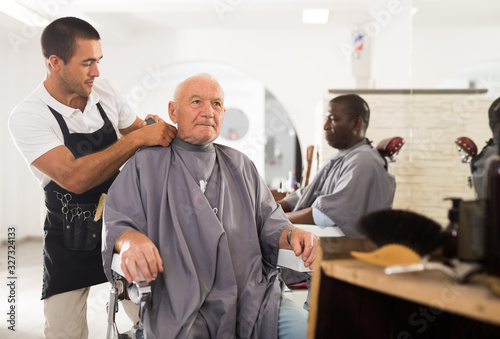 Barber putting on hairdresser cloak to elderly male client