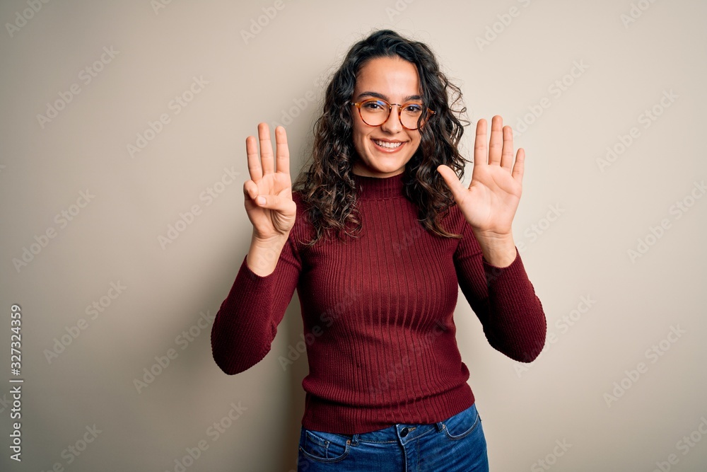 Beautiful woman with curly hair wearing casual sweater and glasses over white background showing and pointing up with fingers number eight while smiling confident and happy.
