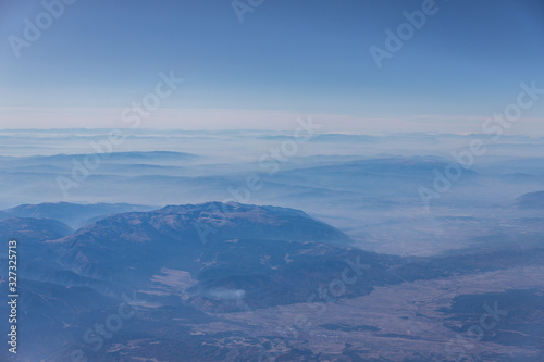 View from the aircraft window on the way to Crete, flying over Greece. There are mountain peaks and blue sky in frame. 