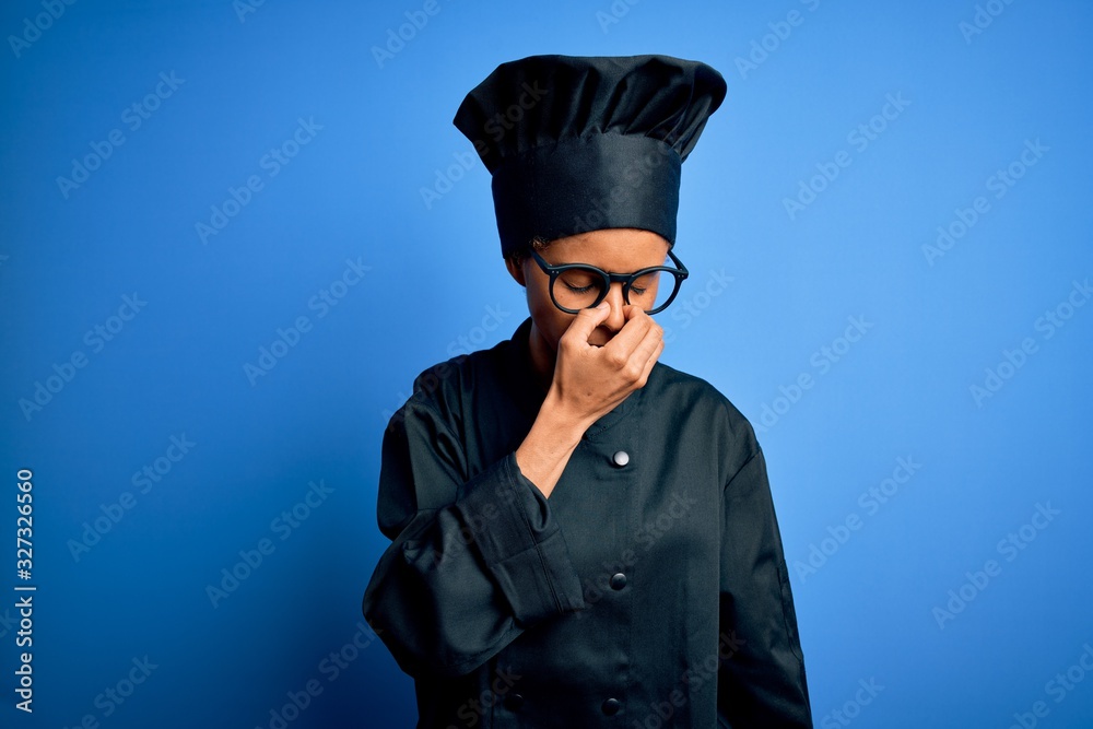 Young african american chef woman wearing cooker uniform and hat over blue background tired rubbing nose and eyes feeling fatigue and headache. Stress and frustration concept. Young african american chef woman wearing cooker uniform and hat over blue background tired rubbing nose and eyes feeling fatigue and headache. Stress and frustration concept.