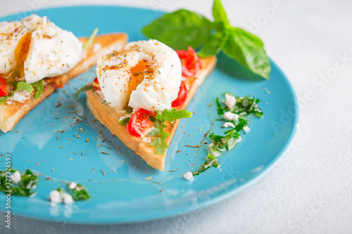 Two poached eggs on toasted toast with cherry tomatoes, cheese and herbs on a large blue plate