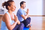 Middle age beautiful sporty couple sitting on mat practicing yoga doing prayer pose at gym