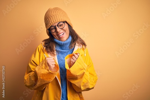 Middle age woman wearing yellow raincoat and winter hat over isolated background excited for success with arms raised and eyes closed celebrating victory smiling. Winner concept. © Krakenimages.com