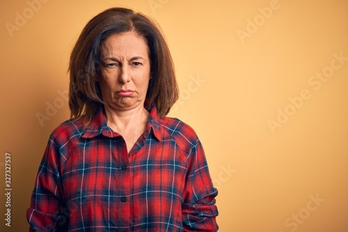 Middle age beautiful woman wearing casual shirt standing over isolated yellow background depressed and worry for distress, crying angry and afraid. Sad expression.
