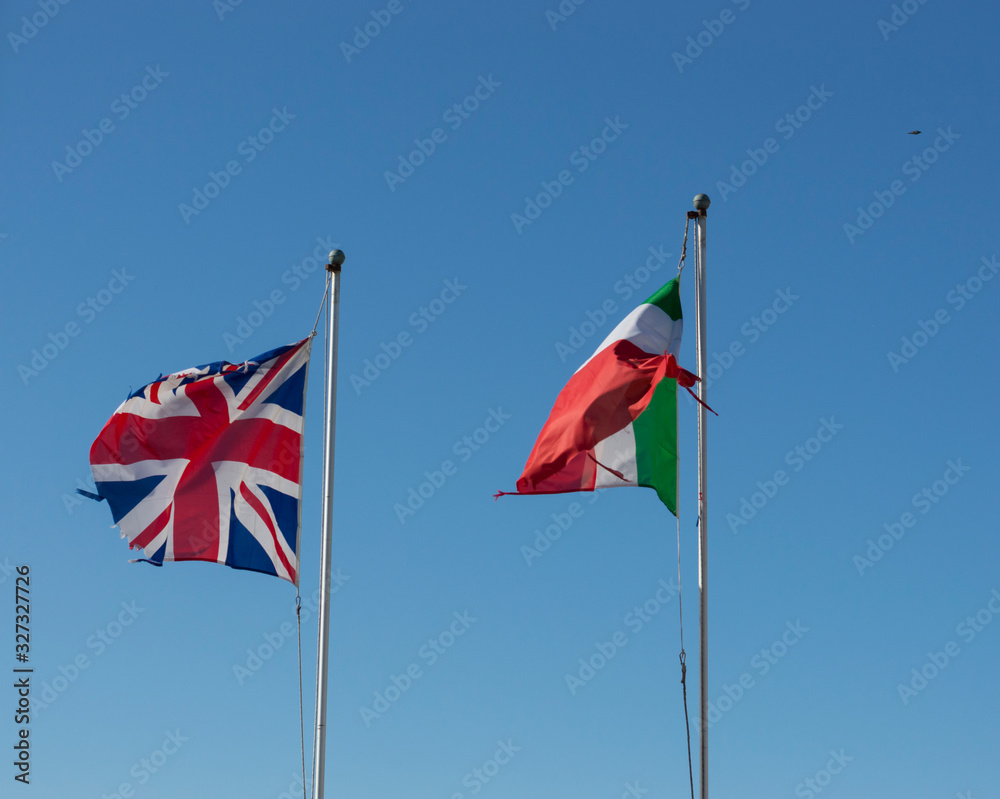Flags of the UK and Italy waving on background of blue sky