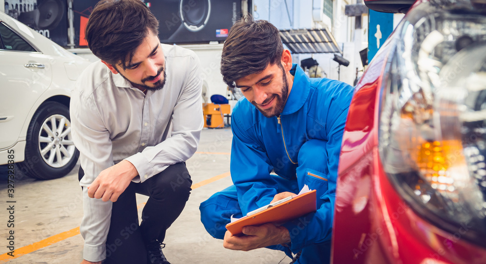 Mechanic holding clipboard with car owner in the workshop garage. Car auto services concepts Mechanic holding clipboard with car owner in the workshop garage. Car auto services concepts