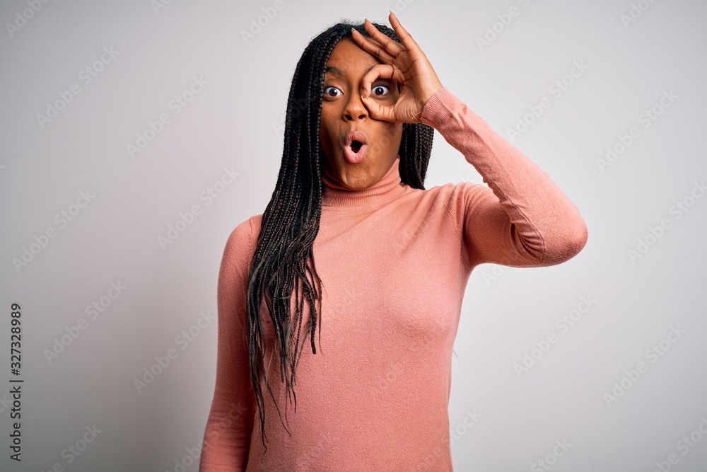 Fototapeta premium Young african american woman standing casual and cool over white isolated background doing ok gesture shocked with surprised face, eye looking through fingers. Unbelieving expression.