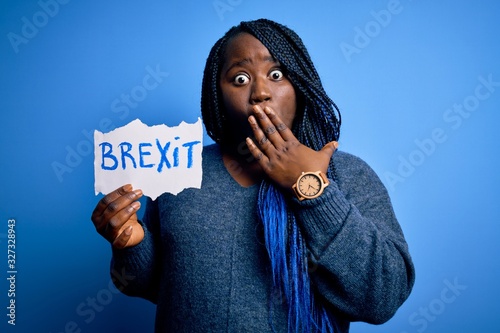 Young african american plus size woman with braids holding paper with brexit message cover mouth with hand shocked with shame for mistake, expression of fear, scared in silence, secret concept photo