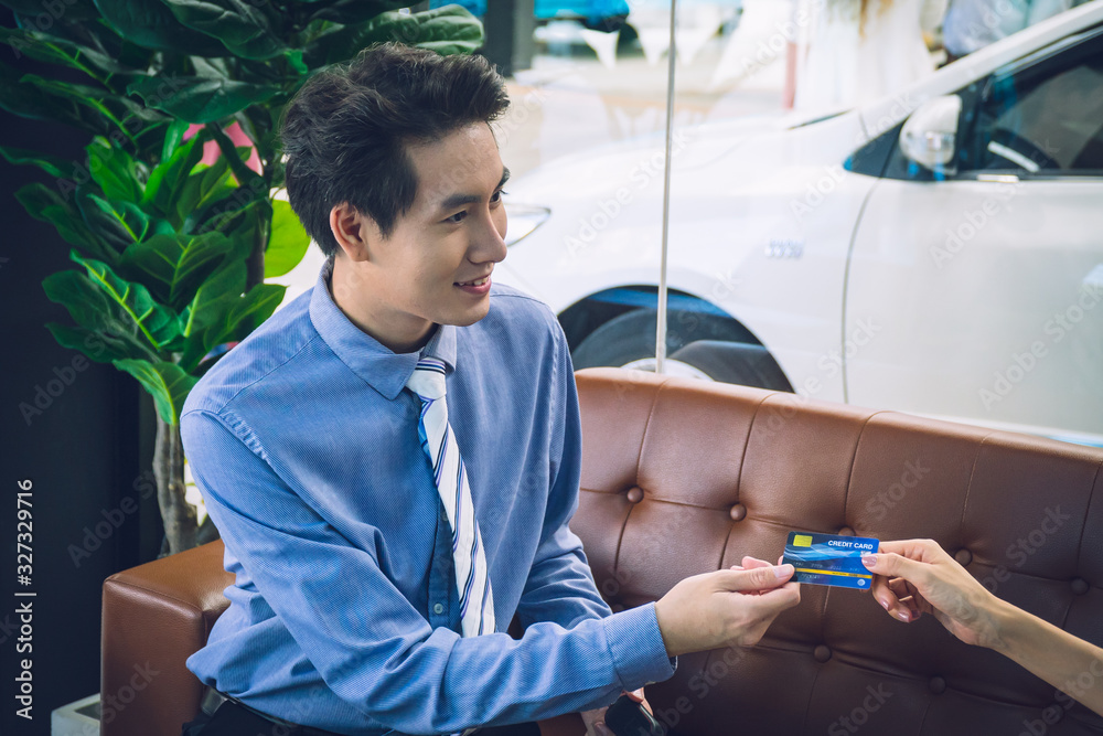 Car salesman receiving credit card from youn attractive girl in the car