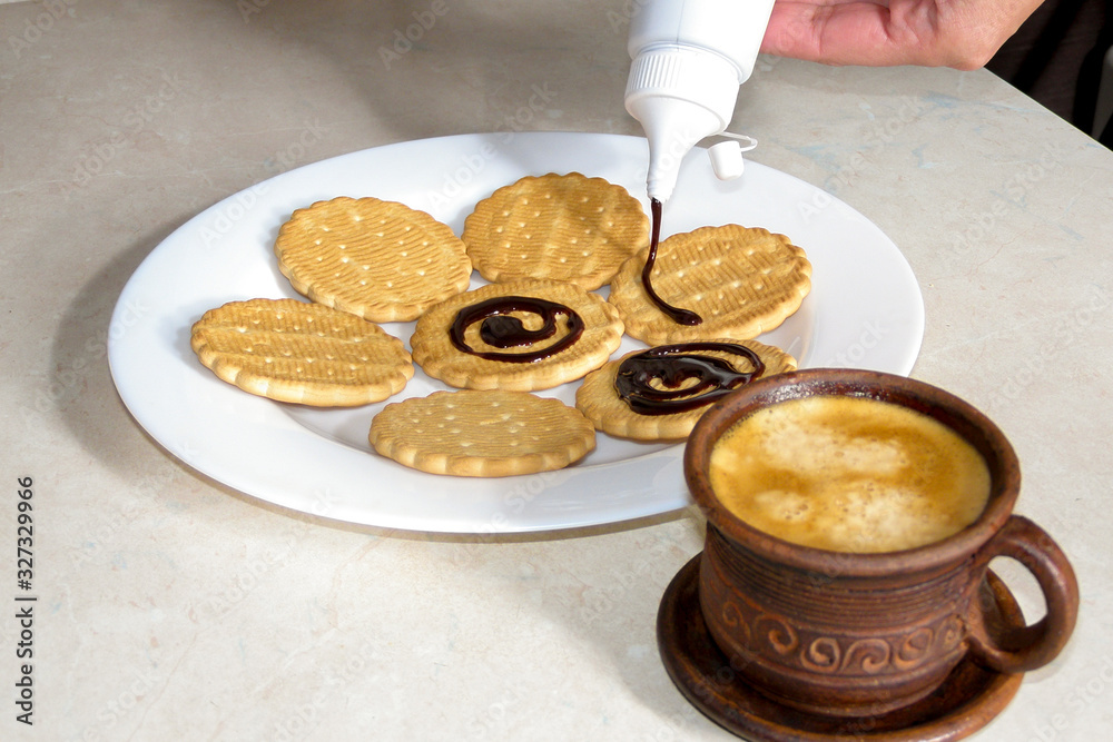 Chocolate decorated cookies laid out on a white plate. A cup of coffee. Chocolate decorated cookies laid out on a white plate. A cup of coffee.