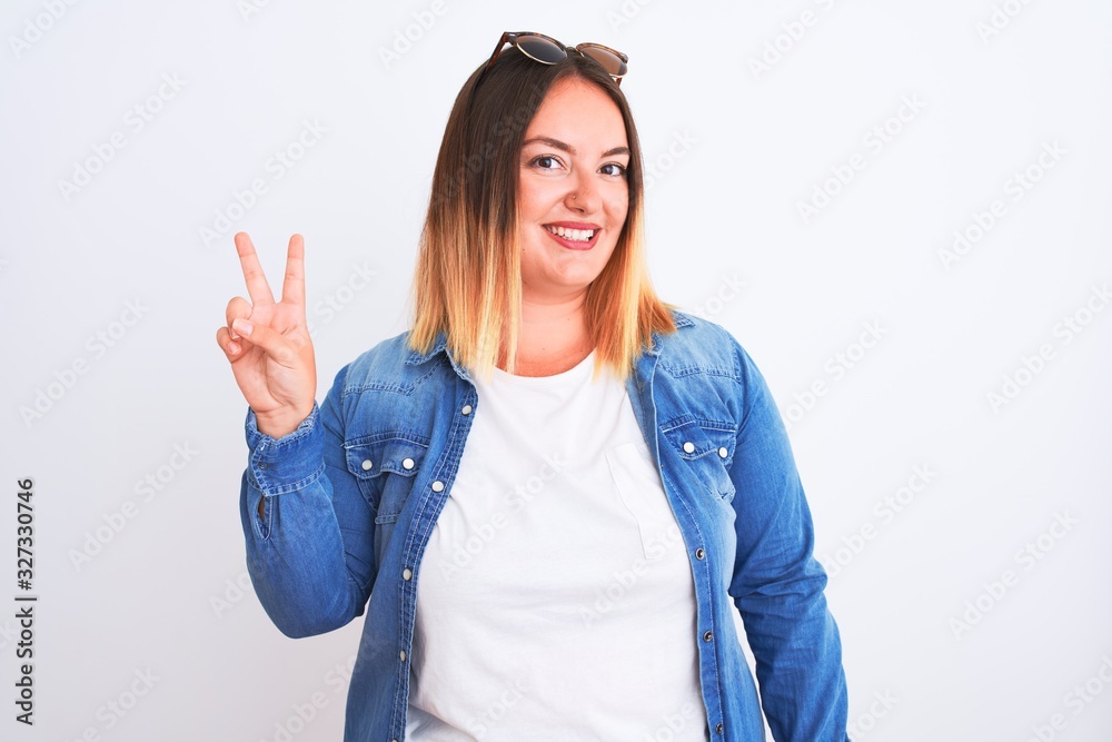 Beautiful woman wearing denim shirt standing over isolated white background smiling with happy face winking at the camera doing victory sign with fingers. Number two.