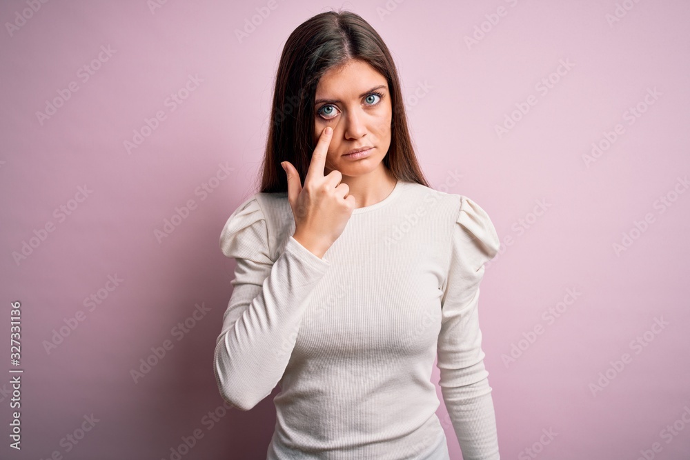Young beautiful woman with blue eyes wearing casual white t-shirt over pink background Pointing to the eye watching you gesture, suspicious expression Young beautiful woman with blue eyes wearing casual white t-shirt over pink background Pointing to the eye watching you gesture, suspicious expression