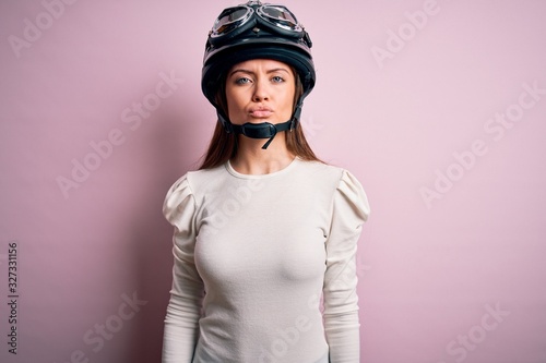Young beautiful motorcyclist woman with blue eyes wearing moto helmet over pink background looking at the camera blowing a kiss on air being lovely and sexy. Love expression.
