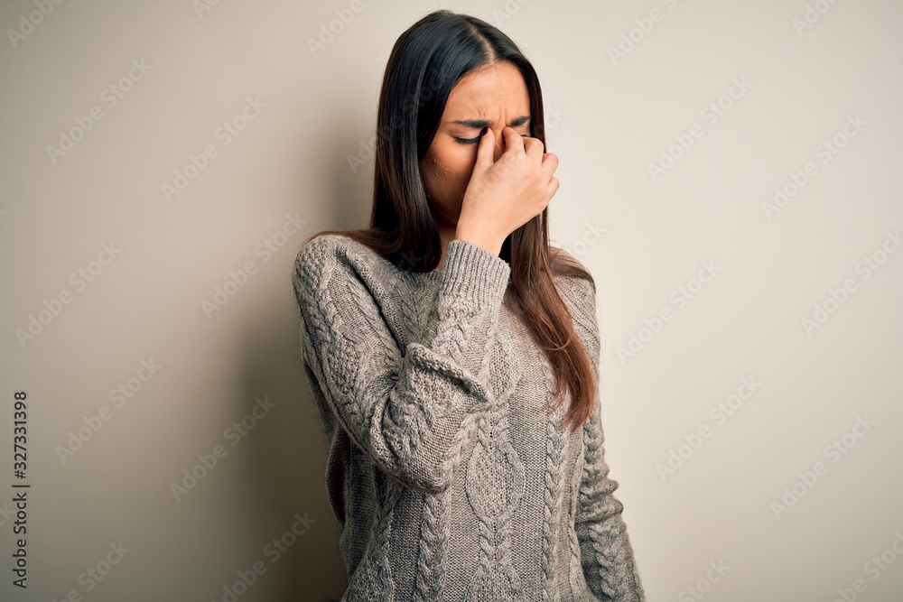 Young beautiful brunette woman wearing casual sweater over isolated white background tired rubbing nose and eyes feeling fatigue and headache. Stress and frustration concept. Young beautiful brunette woman wearing casual sweater over isolated white background tired rubbing nose and eyes feeling fatigue and headache. Stress and frustration concept.