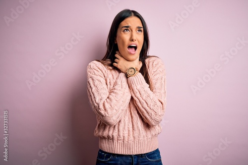 Young beautiful brunette woman wearing casual sweater over isolated pink background shouting suffocate because painful strangle. Health problem. Asphyxiate and suicide concept. © Krakenimages.com